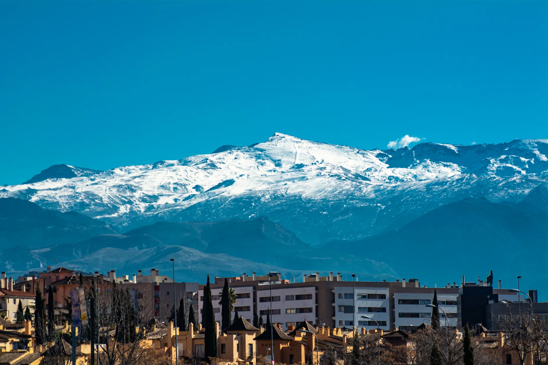 Panoramic view of snowy Sierra Nevada mountains towering over Granada's urban landscape.