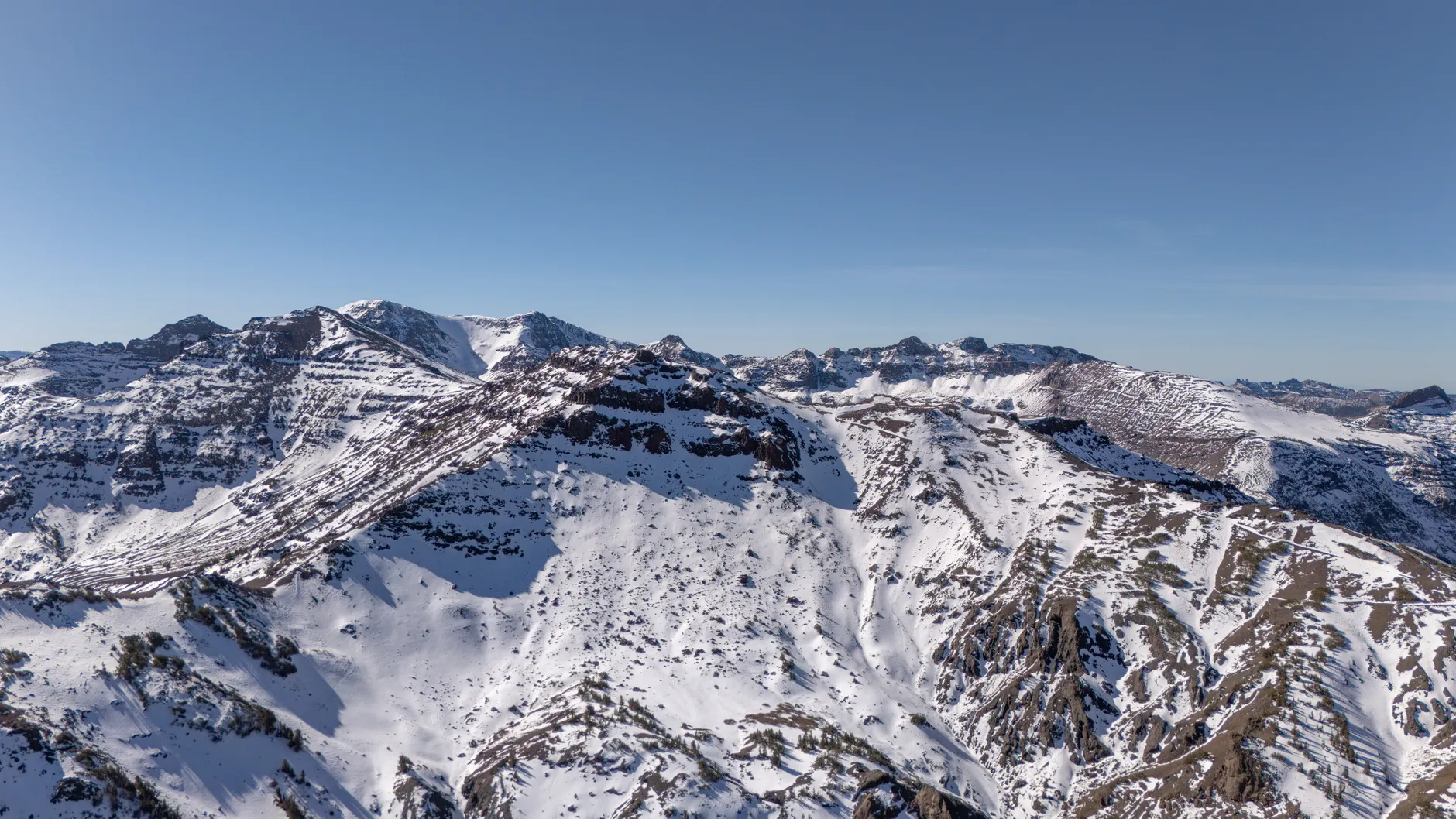 Breathtaking aerial photograph capturing the snow-covered Sierra Nevada mountains under a clear blue sky.